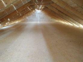 Surowe poddasze z drewnianą konstrukcją dachu i podłogą z płyt OSB, przygotowane do dalszych prac wykończeniowych.