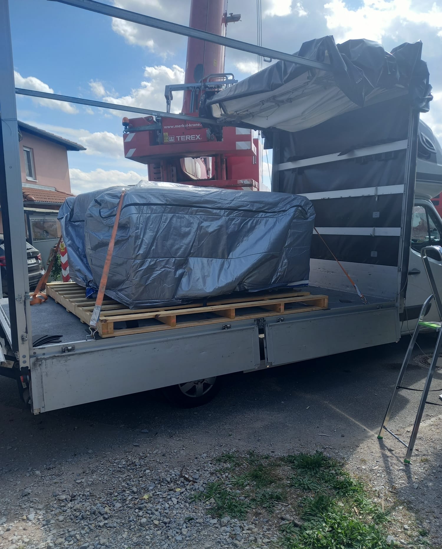 Załadunek dużego, owiniętego folią przedmiotu na palecie do otwartego busa z pomocą dźwigu Terex.