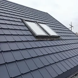 Szary dach z blachy trapezowej z dwoma oknami dachowymi, widoczne połączenia blach i mocowania.