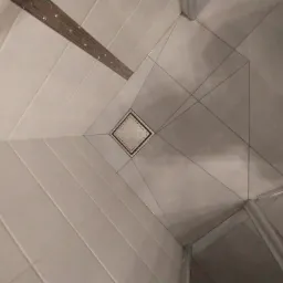 Wykończona podłoga prysznica z odpływem liniowym i kwadratowym odpływem punktowym, płytki ułożone pod kątem.