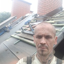 Bogusław Rabiej - Mężczyzna robiący selfie na dachu podczas prac dekarskich, widoczne kominy z cegły i drabina dekarska