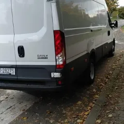 Tył białego busa Iveco Daily zaparkowanego na ulicy, widoczne jesienne liście na chodniku.