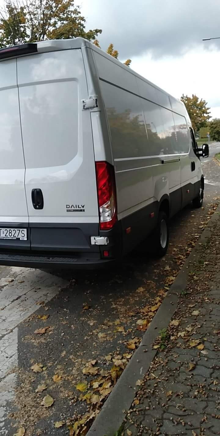 Tył białego busa Iveco Daily zaparkowanego na ulicy, widoczne jesienne liście na chodniku.