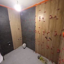 Ter-Bud - Montaż płytek ściennych w łazience, widoczne płytki w dwóch kolorach, system poziomowania płytek, przygotowane otwory na instalacje, na podłodze leżą narzędzia glazurnicze.