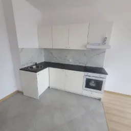 Nowoczesna, jasna kuchnia z białymi szafkami, czarnym blatem i marmurowym backsplashiem, widok z góry, sylikon w tubie na półce nad okapem.