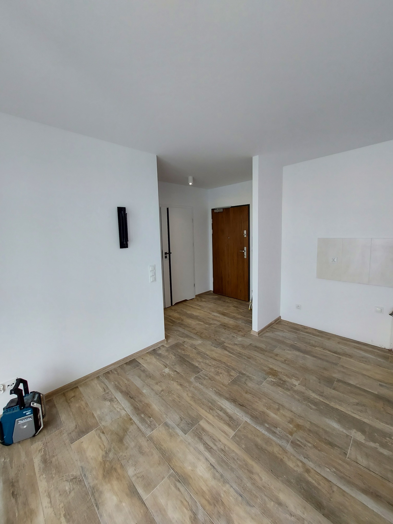 Wnętrze mieszkania w Pruszczu Gdańskim z ułożoną podłogą z płytek imitujących drewno, widoczny głośnik budowlany Makita w rogu pomieszczenia.