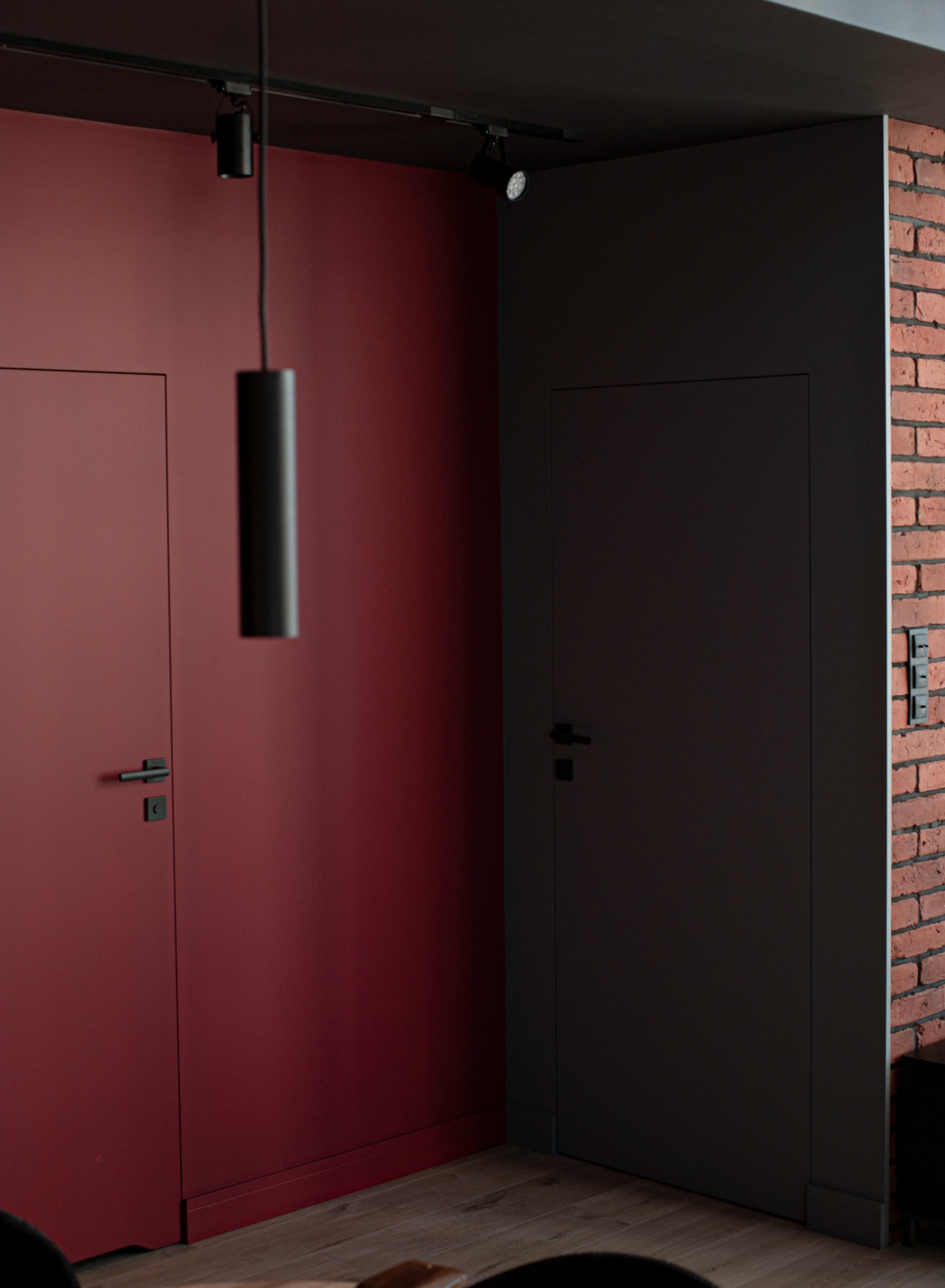 Dwa nowoczesne, minimalistyczne skrzydła drzwiowe: bordowe i grafitowe, zamontowane w mieszkaniu w Pruszczu Gdańskim. Bordowe drzwi na tle bordowej ściany, grafitowe drzwi sąsiadują z fragmentem...