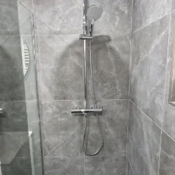 Nowoczesna kabina prysznicowa z deszczownicą i szarymi płytkami imitującymi marmur, czarny brodzik z odpływem liniowym, szklana ściana kabiny