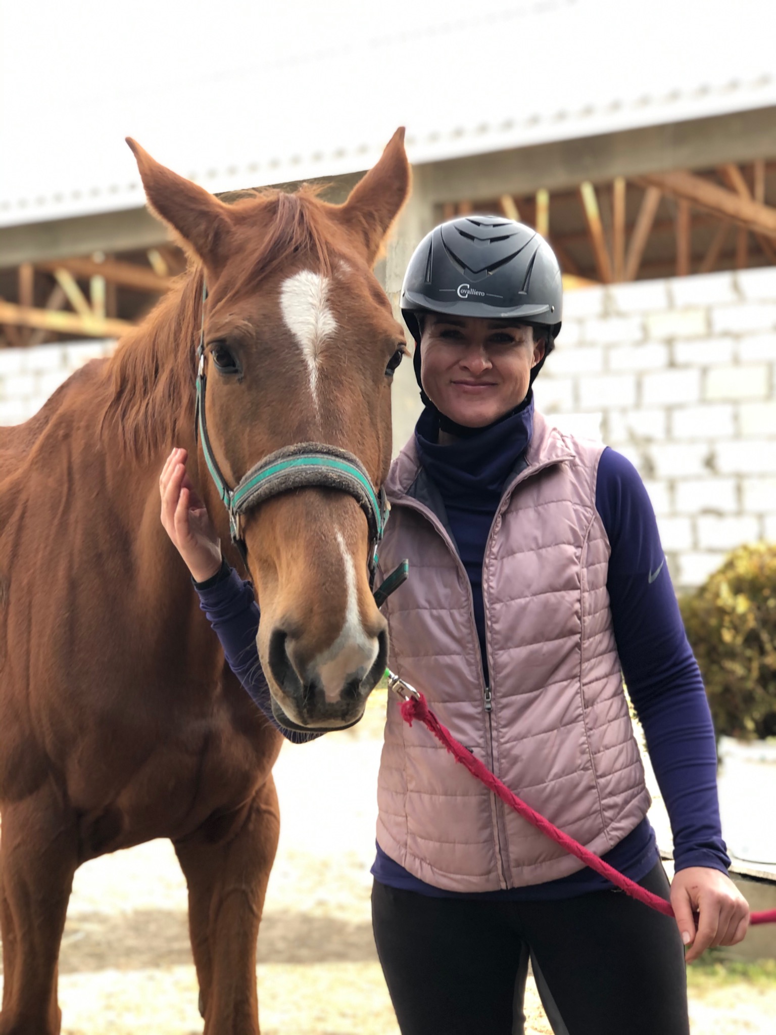 Kobieta w kasku z koniem kasztanowym z białą strzałką na czole, trzymająca czerwoną uwiąz.