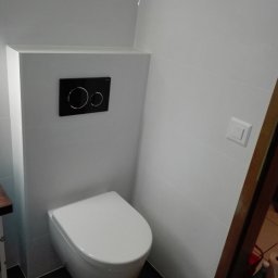 Remart - Nowoczesna toaleta wisząca z czarnym panelem spłukującym na tle białych płytek ściennych i ciemnej podłogi.