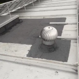 Płaski dach pokryty szarą papą z turbiną wentylacyjną i panelami słonecznymi, widok z góry.