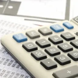 Kalkulator, ołówek automatyczny i arkusz kalkulacyjny z liczbami w tle, ujęcie z góry.