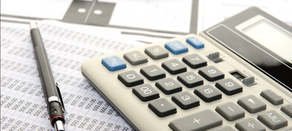 Kalkulator, ołówek automatyczny i arkusz kalkulacyjny z liczbami w tle, ujęcie z góry.