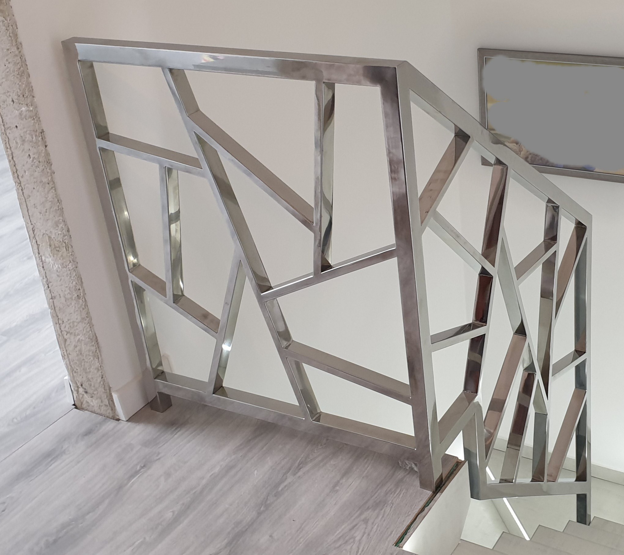 Nowoczesna balustrada schodowa ze stali nierdzewnej o geometrycznym wzorze, widok z góry na marmurowe schody.