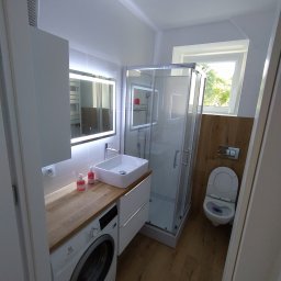 Bodzio. Remonty - Nowoczesna łazienka z kabiną prysznicową, toaletą i umywalką nablatową na drewnianym blacie, pod którym znajduje się pralka; oświetlenie LED w lustrze.