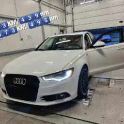 Białe Audi A6 na hamowni w Radomiu, z otwartymi drzwiami kierowcy, widoczne wyniki pomiaru mocy i momentu obrotowego na ścianie warsztatu.