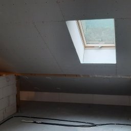 Zir-bud Ruslan Zirchak - Poddasze w trakcie adaptacji: ściana z bloczków, zamontowana płyta gipsowo-kartonowa na skosach dachu z oknem dachowym, widoczne przewody elektryczne na podłodze.