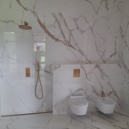 Zir-bud Ruslan Zirchak - Wykończona łazienka w Halinowie z białymi płytkami imitującymi marmur z brązowymi żyłami, złotą armaturą, wiszącą toaletą i bidetem.