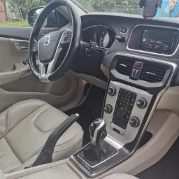 Wnętrze samochodu Volvo z jasną skórzaną tapicerką, widoczna deska rozdzielcza, kierownica z logo Volvo, dźwignia zmiany biegów i uchwyt na telefon.