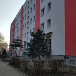 ARTEX 2.0 Sp.zo.o. - Wielopiętrowy budynek po renowacji elewacji, z szarymi ścianami i czerwonymi pasami, widoczny z poziomu chodnika. Uwagę zwracają małe drzewka przed budynkiem.