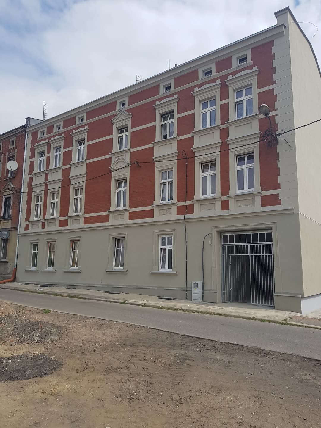 Odnowiona, trzypiętrowa kamienica w Rudzie Śląskiej z czerwoną cegłą na górnych piętrach i szarą farbą na dole. Widoczne odświeżone okna i elewacja.