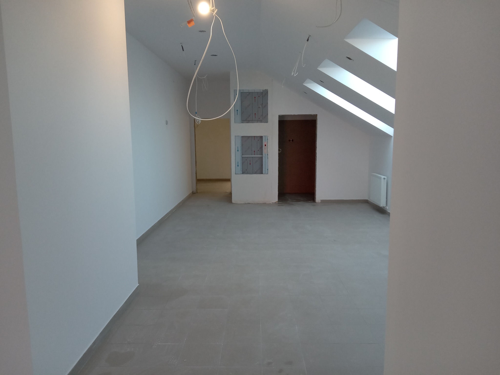 Poddasze po remoncie z oknami dachowymi, szarą podłogą z płytek, białymi ścianami i instalacją elektryczną do wykończenia.