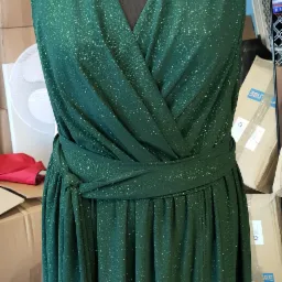 Błyszcząca, szmaragdowa sukienka z kopertowym dekoltem i wiązaniem w pasie, zaprezentowana na czarnym manekinie krawieckim. Widoczny rozporek na dole sukienki.