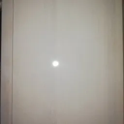 Jasny, lakierowany panel drewniany z delikatnym rysunkiem słojów, odbijający światło w centralnej części, z widoczną krawędzią po lewej stronie.