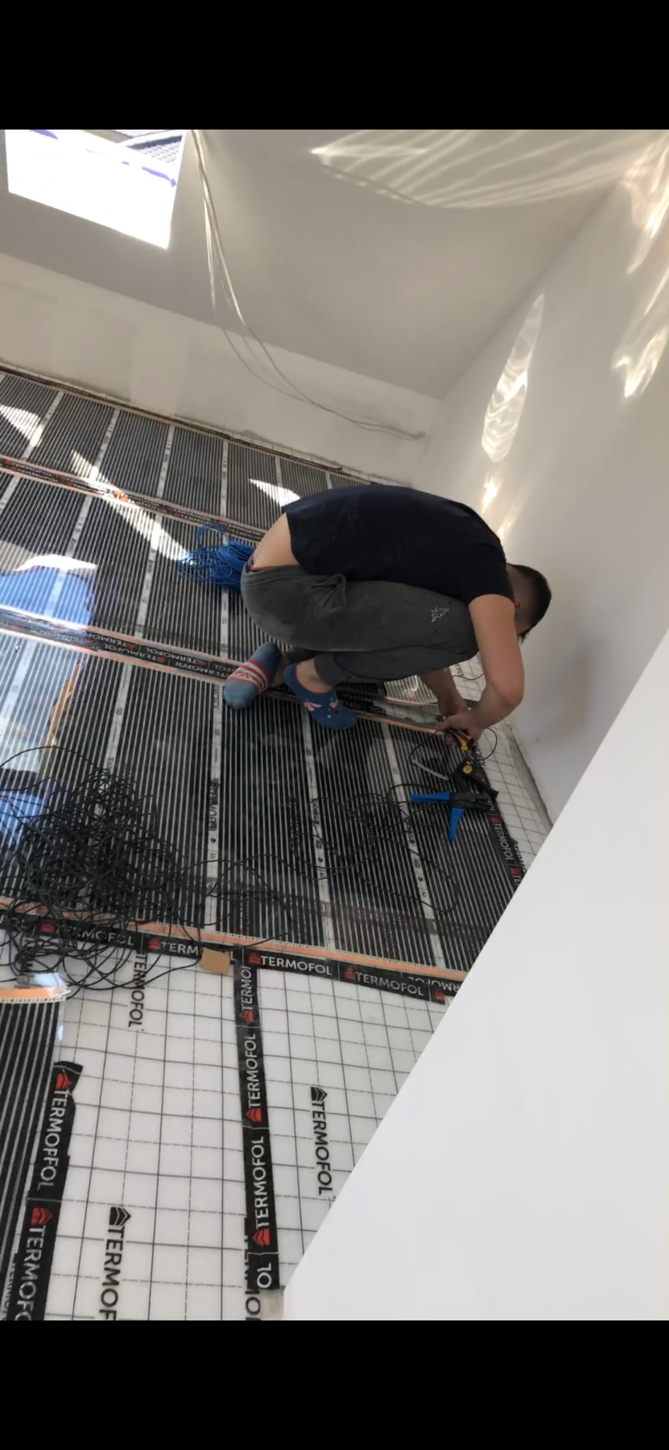 Monter w trakcie instalacji ogrzewania podłogowego elektrycznego marki Termofol, widoczne maty grzewcze z przewodami, narzędzia i niebieski przewód zasilający.