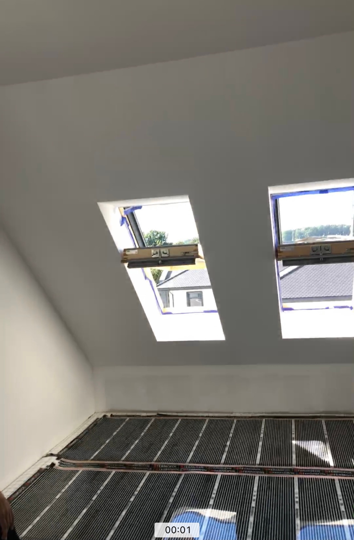 Montaż folii grzewczej na podłodze poddasza z oknami dachowymi, widoczne elementy instalacji elektrycznej i izolacji.