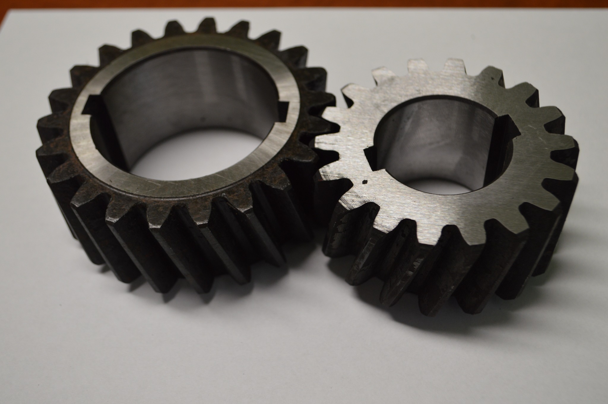 Dwie metalowe zębatki o różnej wielkości, leżące na białym tle, wykonane w Raszowej.