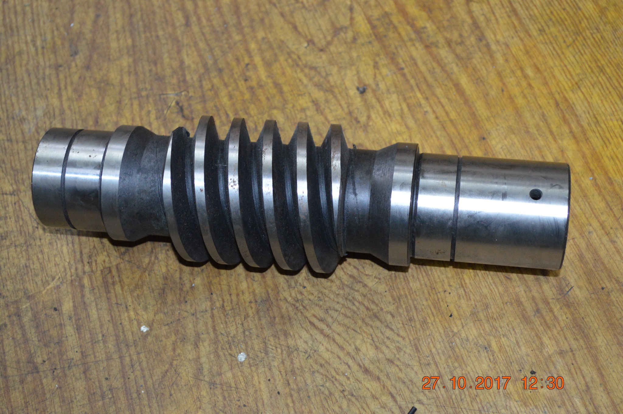 Metalowa śruba ślimakowa z wyraźnymi śladami obróbki na tle drewnianego blatu roboczego.