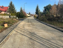 Nowa droga z jasnym kruszywem w wiejskiej scenerii. Świeżo wykonane obrzeża, słoneczny dzień, widok z perspektywy osoby stojącej na początku drogi.