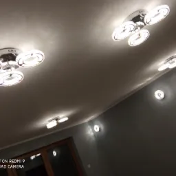 Nowoczesne oświetlenie sufitowe z okrągłymi lampami LED w szarym pokoju, widok z dołu, ciepłe światło odbijające się od sufitu.