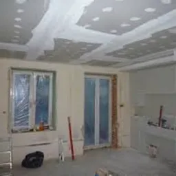 Wnętrze po montażu płyt kartonowo-gipsowych na suficie i ścianach, widoczne łączenia płyt zaszpachlowane, okna zabezpieczone folią malarską, pomieszczenie przygotowane do dalszych prac...