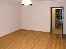 Pusty pokój po remoncie z drewnianą podłogą, świeżo pomalowane ściany w odcieniach beżu, widoczny otwarty pokój w tle z oknem.