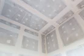 Wnętrze pomieszczenia w trakcie wykańczania, widok na sufit i górne partie ścian z widocznymi łączeniami płyt, częściowo pokrytymi masą szpachlową, przygotowanymi do dalszej obróbki.