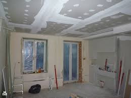 Wnętrze po montażu płyt kartonowo-gipsowych na suficie i ścianach, widoczne łączenia płyt zaszpachlowane, okna zabezpieczone folią malarską, pomieszczenie przygotowane do dalszych prac...