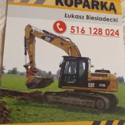 Ujęcie ulotki reklamowej usług koparką CAT 319D, z numerem telefonu i informacją o Łukaszu Biesiadeckim, na tle zielonej trawy i drzew.