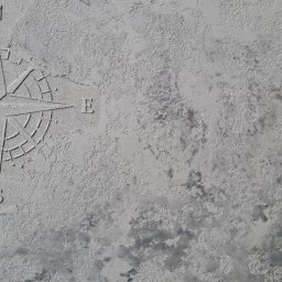 IVAD - Szara ściana z fakturą imitującą mapę świata i wkomponowaną w nią różą wiatrów, wykonana techniką dekoracyjnego tynkowania.