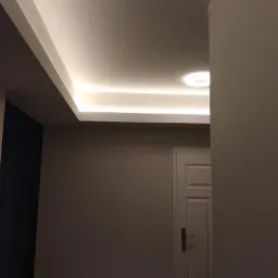 Nowoczesne oświetlenie sufitowe z listwami LED w korytarzu z białą ścianą i drzwiami.