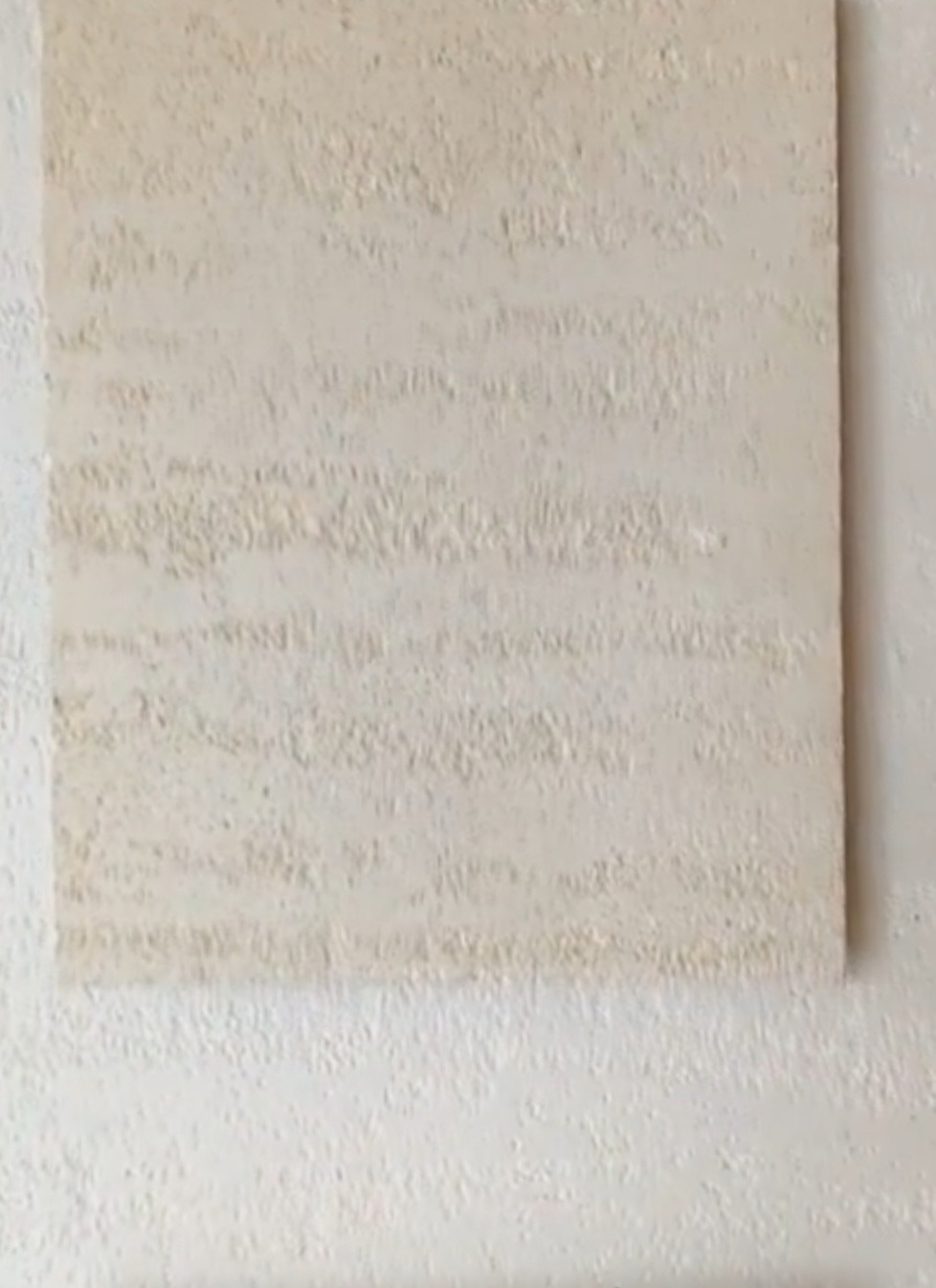 Fragment ściany z dekoracyjnym, beżowym tynkiem strukturalnym o wyraźnej, poziomej fakturze, przylegający do gładkiej, białej ściany.