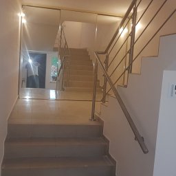 prywatnie - Klatka schodowa z lustrzaną ścianą i metalową balustradą; widoczny panel alarmowy na białej ścianie.