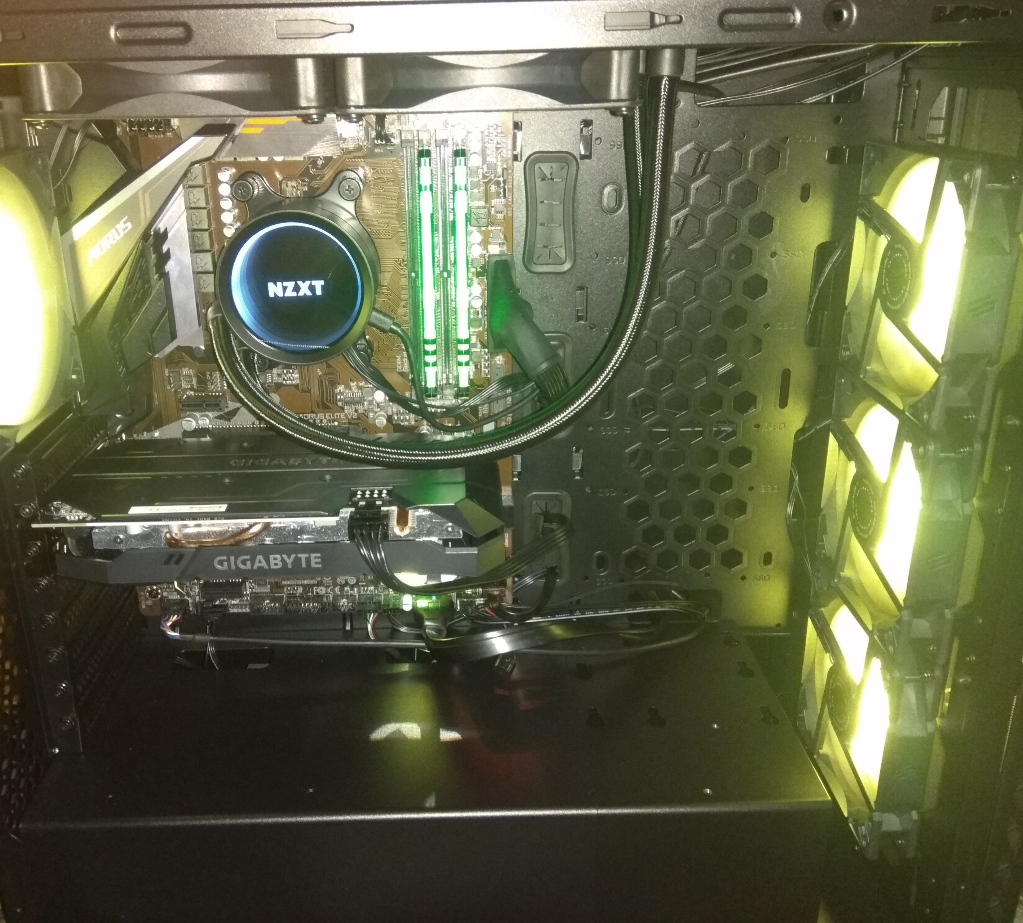 Wnętrze obudowy komputera stacjonarnego z podświetleniem LED, widoczna karta graficzna Gigabyte, chłodzenie wodne NZXT oraz wentylatory z żółtym podświetleniem.