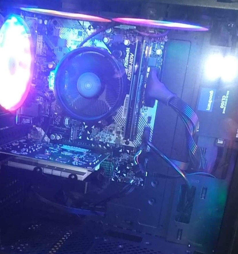 Wnętrze komputera stacjonarnego z podświetleniem LED, widoczna płyta główna ASRock A320M-HDV, karta graficzna i dysk SSD Goodram CL100, chłodzenie procesora z wentylatorem.