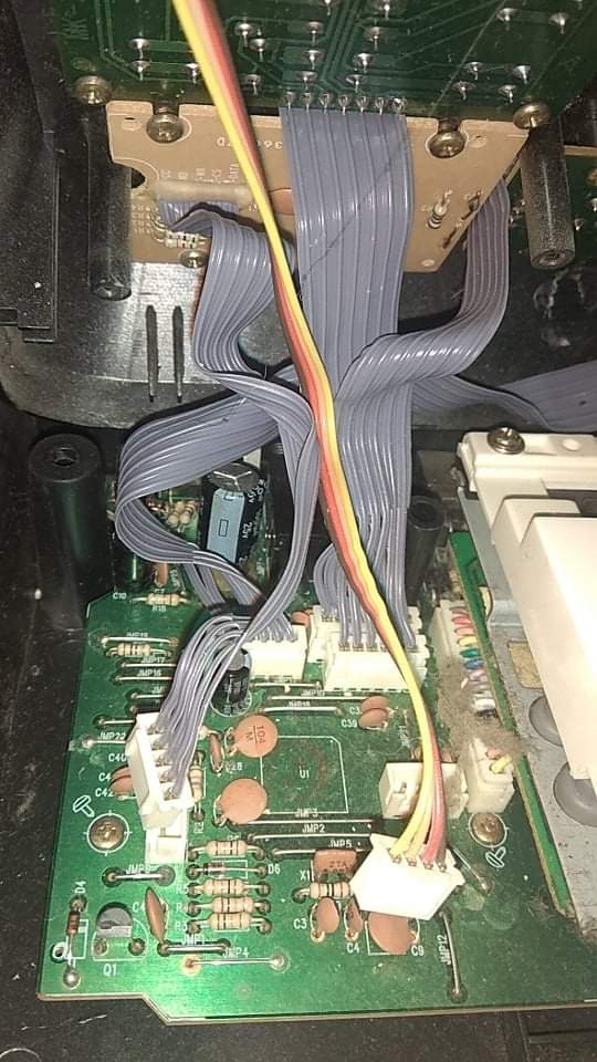 Otwarta obudowa urządzenia elektronicznego z widoczną zieloną płytą główną, licznymi kablami taśmowymi i przewodami w kolorach żółtym, czerwonym i brązowym, podłączonymi do złączek. Widoczne...