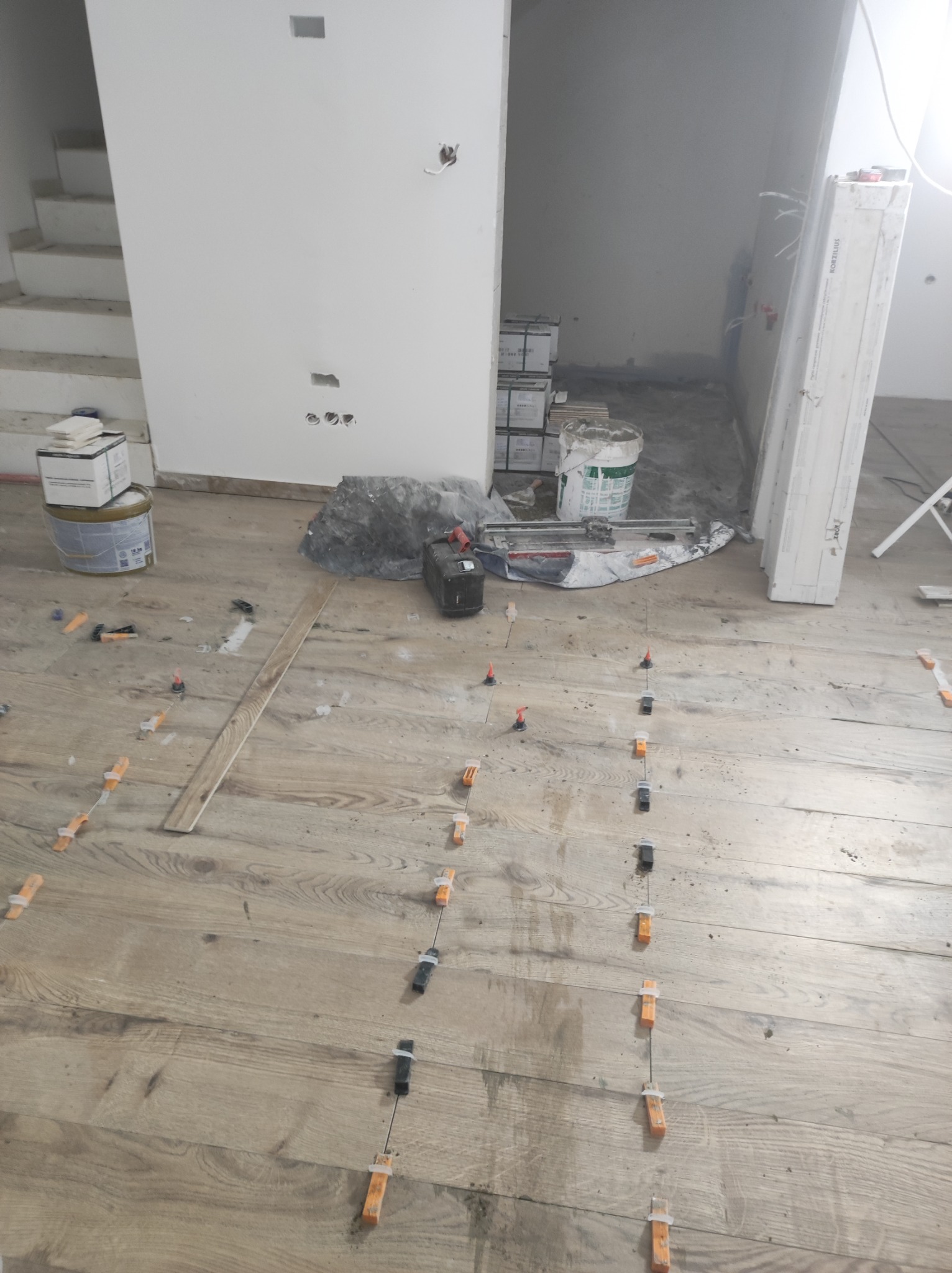 Układanie podłogi drewnopodobnej z użyciem klipsów poziomujących, widoczne narzędzia i materiały budowlane w tle.