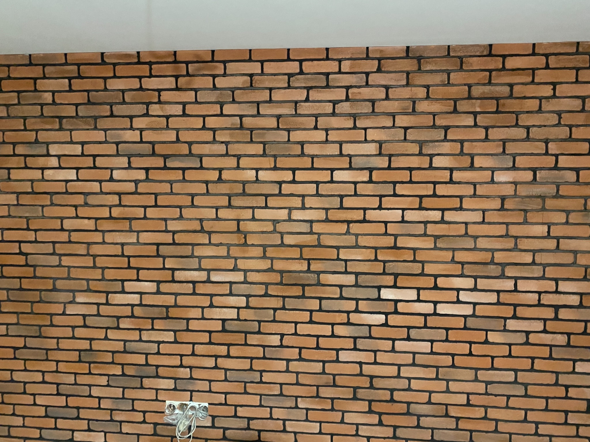 Ściana wykończona cegłą klinkierową w odcieniach brązu i beżu, z widocznym gniazdkiem elektrycznym w dolnej części.