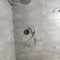 Nowoczesna łazienka z deszczownicą i panelem prysznicowym, wykończona płytkami w odcieniach szarości i drewnopodobną podłogą z odpływem liniowym.