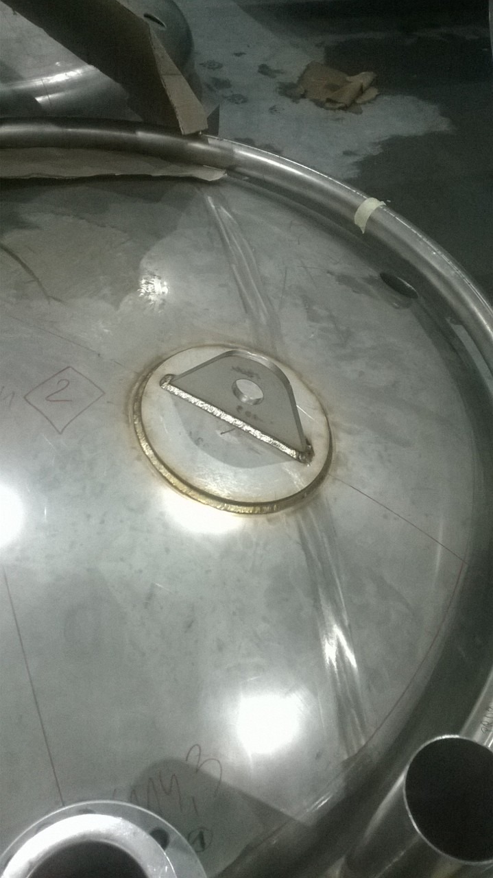 Wnętrze zbiornika ze stali nierdzewnej z przyspawanym elementem montażowym, widoczne ślady po spawaniu i oznaczenia ołówkiem na powierzchni.
